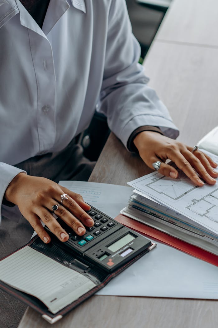 Accountant calculates finances with a calculator and documents on a desk.